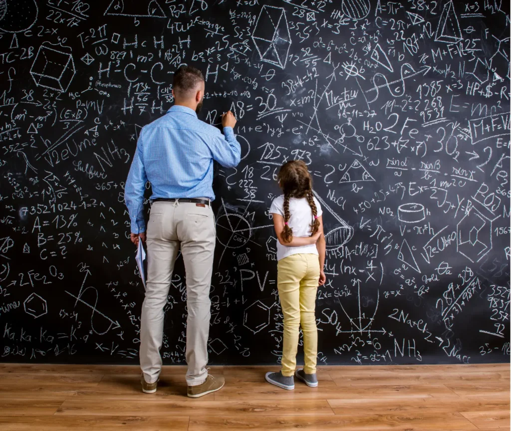 Teacher and young girl standing in front of a chalkboard covered with maths formulas and drawings