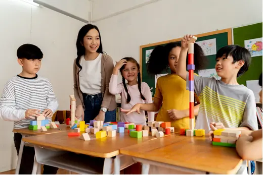 A teacher guiding a group of children building with colourful blocks in a classroom