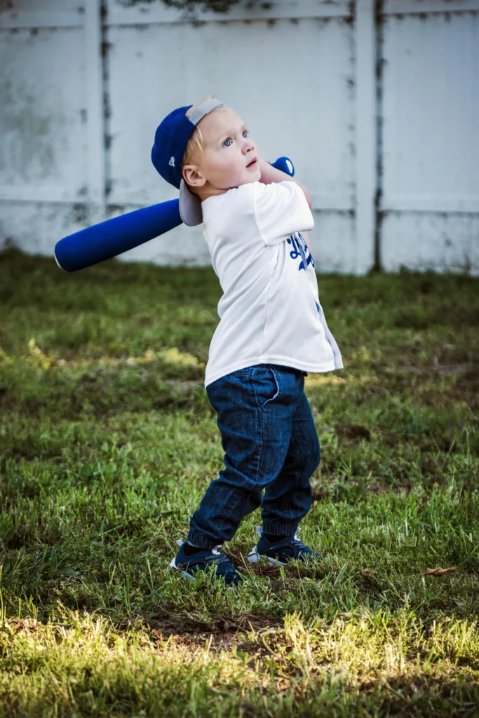 Young child in a cap swinging a blue baseball bat in the yard, a playful introduction to baseball.