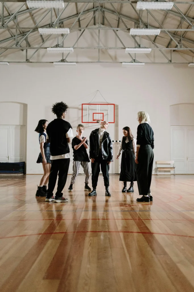 Group of teenagers standing in a gymnasium, rehearsing or performing a drama activity together.
