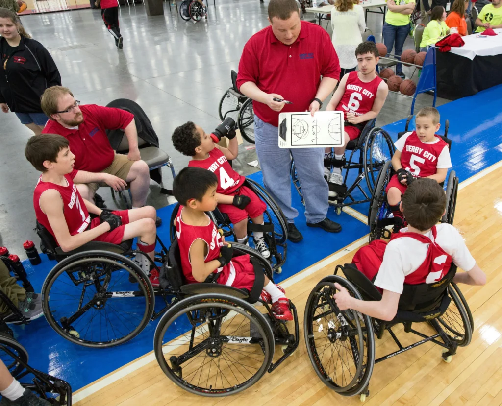 Coach talking to young wheelchair basketball players during a game, highlighting inclusive youth sports and play.