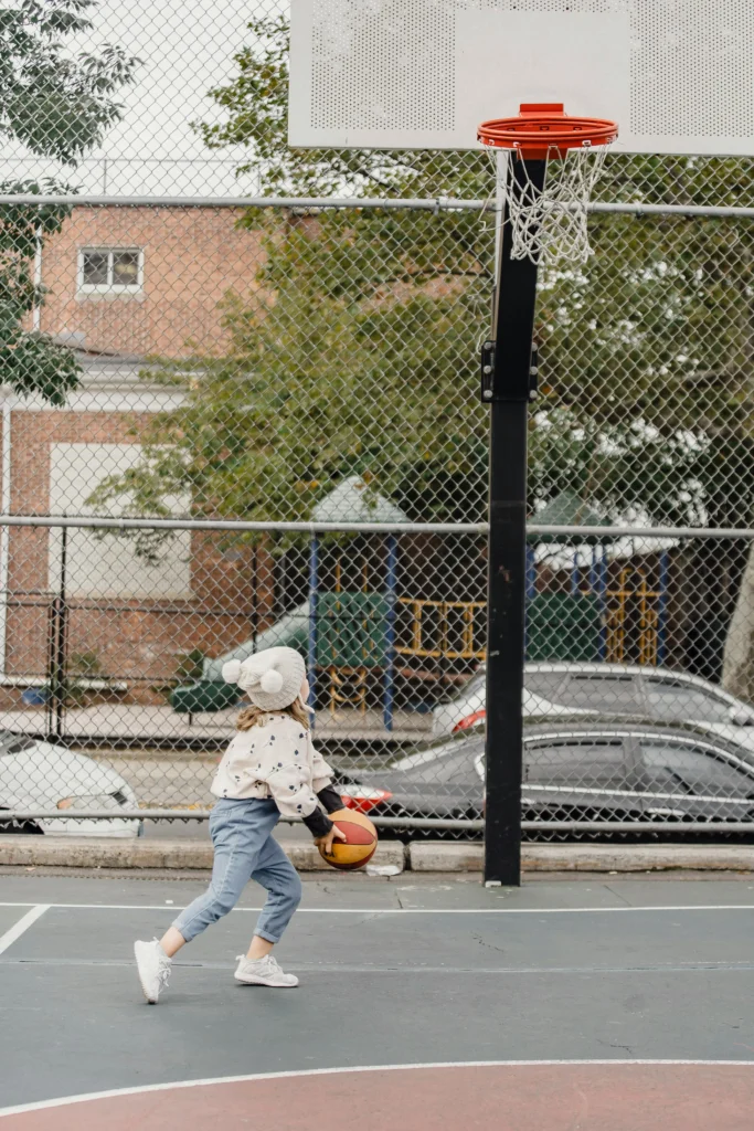 Young girl playing basketball outdoors, preparing to shoot at the hoop.