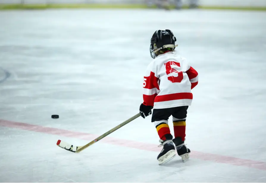 Young child playing ice hockey, skating with the puck during practice.