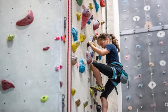 Young girl climbing an indoor rock wall, practicing balance, grip, and coordination.