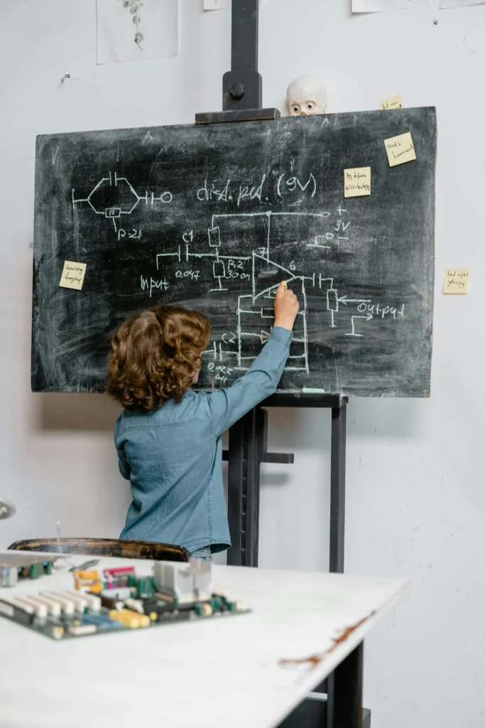 Child drawing technical diagrams and formulas on a blackboard in a classroom setting