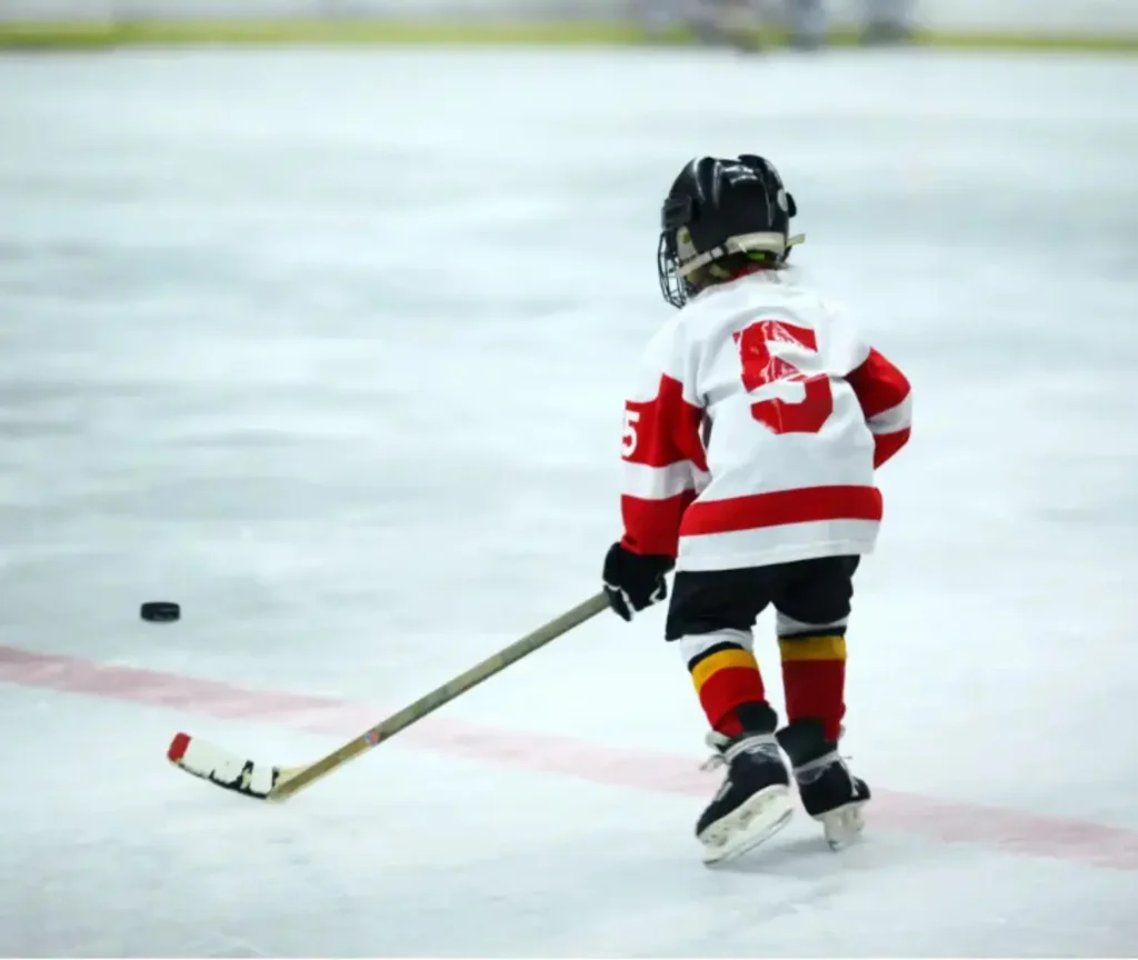 Young child playing ice hockey, skating with the puck during practice.