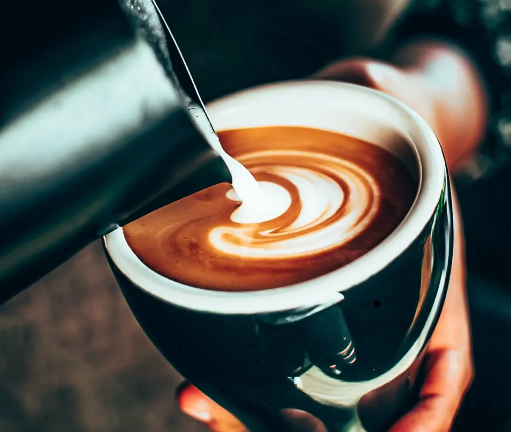 A barista pouring milk into a cup of coffee with latte art