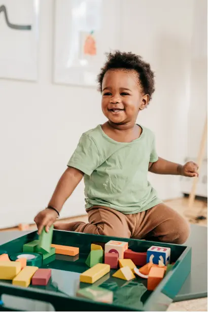 Toddler playing with colorful wooden blocks, developing fine motor skills, spatial awareness, and early problem-solving abilities.