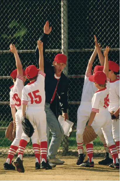 Youth baseball team celebrating with coach during practice