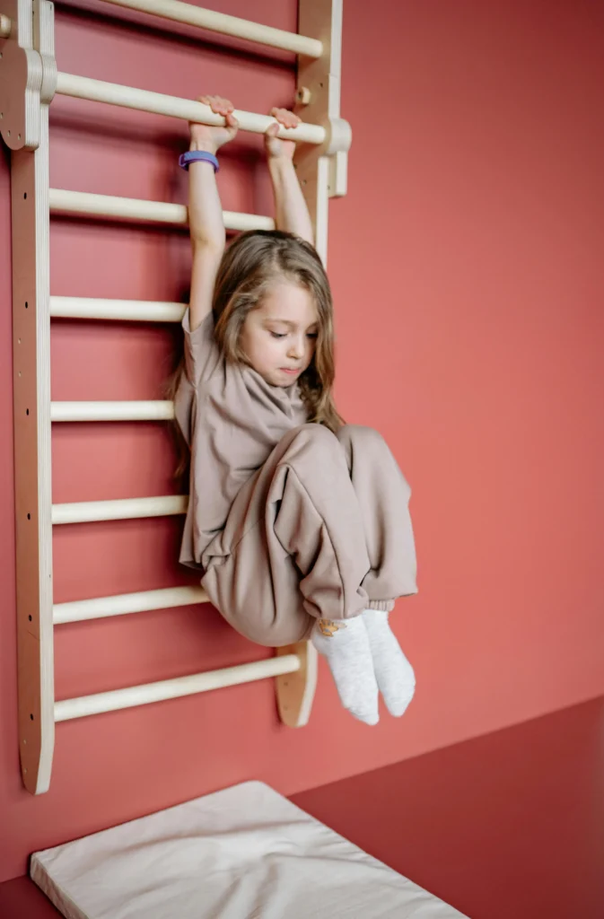 Child hanging from indoor gym bars during physical activity Image Title