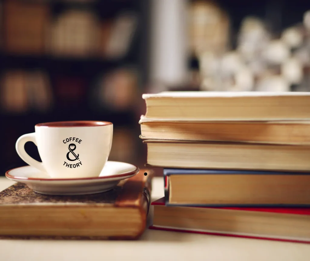 Alt text: Coffee & Theory mug beside a stack of books, representing education research and learning